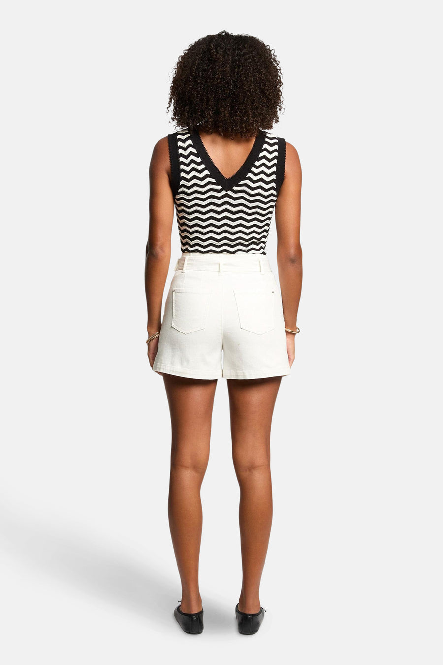 Top sans manches noir, de Morgan de Toi, à motif à rayures géométriques sur une femme portant un short blanc.