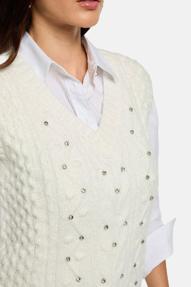 Witte mouwloze top van Morgan de Toi met kabelbreisel, versierd met strass en gedragen over een wit overhemd.