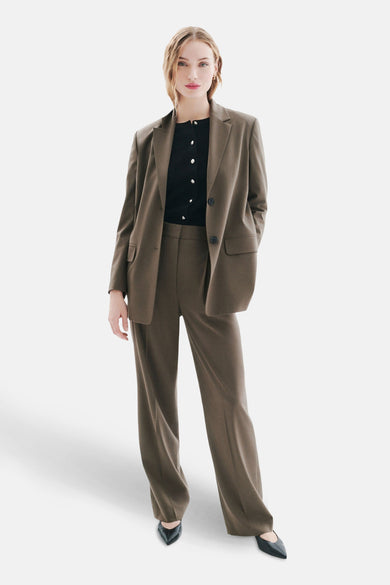 Beige kostuumbroek van Caroll, rechte pasvorm, gedragen met een zwarte cardigan en zwarte puntige pumps.
