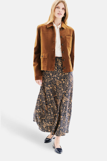 Kort cognac jack van CAROLL, met klepzakken en gedragen over een lange rok met bloemenprint.