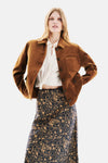 Kort cognackleurig jasje van Caroll, met een witte geknoopte blouse en een lange rok met bloemenprint.
