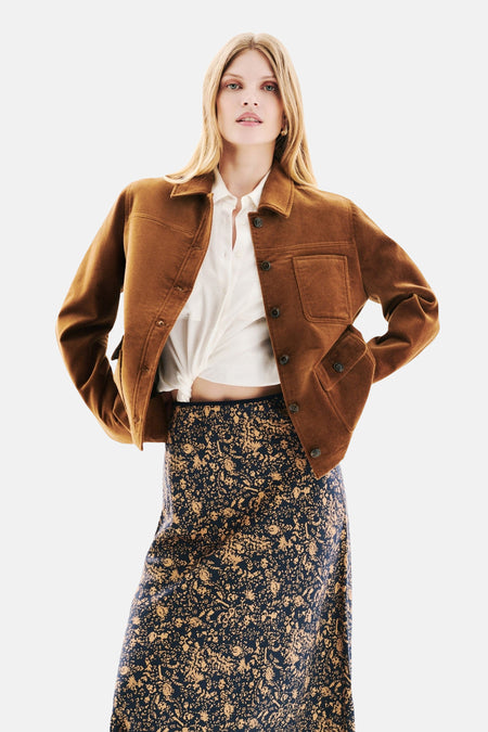 Kort cognackleurig jasje van Caroll, met een witte geknoopte blouse en een lange rok met bloemenprint.
