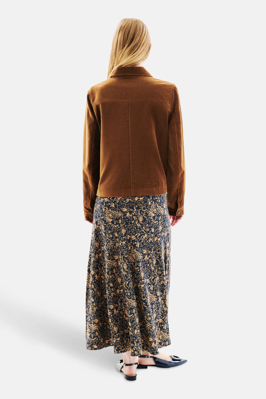 Kort cognacblauw jasje van CAROLL, gedragen met een lange marineblauwe en okerkleurige rok met bloemenprint, van achteren gezien.