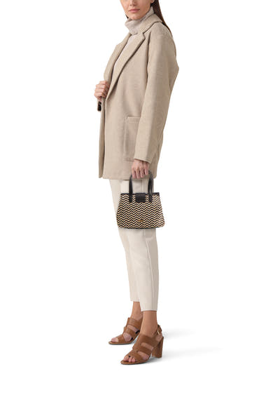 Sac à main noir et beige à motif chevron de Morgan de Toi, en paille avec anses noires, porté de côté.