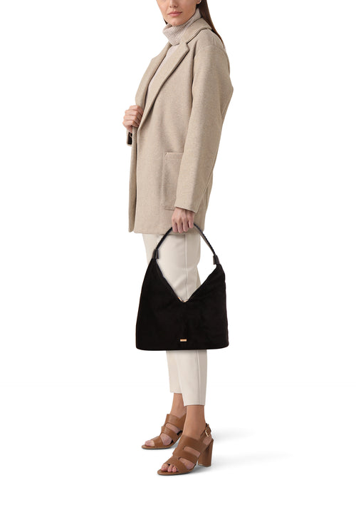 Zwarte schoudertas van Morgan de Toi, gedragen over de schouder met een gevlochten schouderriem, gedragen met een beige jas.