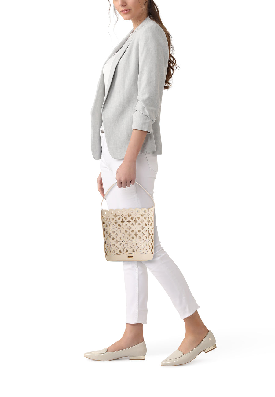Sac à main beige de Morgan de Toi avec motif fleuri découpé, tenu par une femme en blazer gris.
