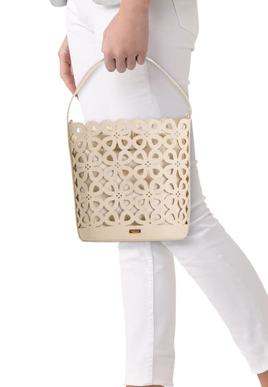 Sac à main beige de Morgan de Toi, avec motif floral découpé, porté par une personne en pantalon blanc.