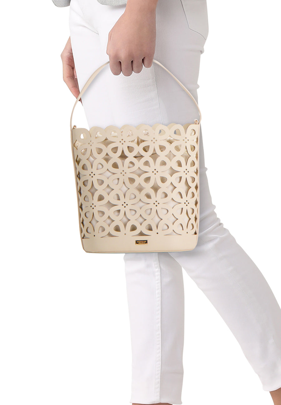 Sac à main beige de Morgan de Toi, avec motif floral découpé, porté par une personne en pantalon blanc.