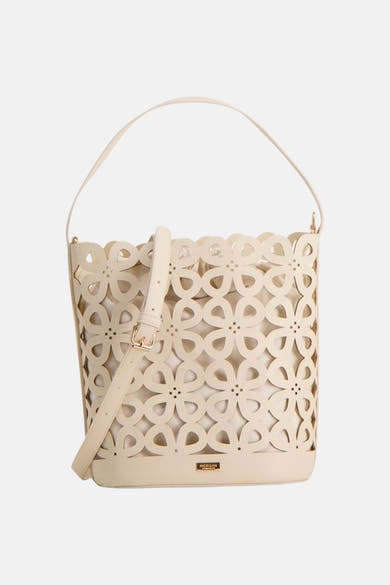 Beige handtas van Morgan de Toi, met uitgesneden bloemenpatroon, gedragen door een persoon in een witte broek.