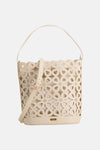 Beige handtas van Morgan de Toi, met uitgesneden bloemenpatroon, gedragen door een persoon in een witte broek.