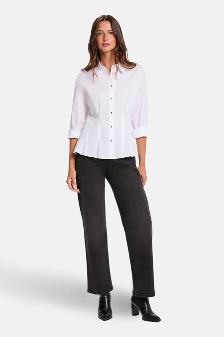 Chemise blanche à manches longues de Morgan de Toi avec boutons et plis décoratifs, portée avec un pantalon noir et des bottes.
