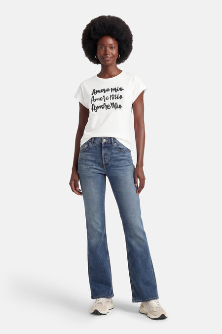 T-shirt blanc à manches courtes de Morgan de Toi, avec motif de texte noir, porté avec un jean bleu.
