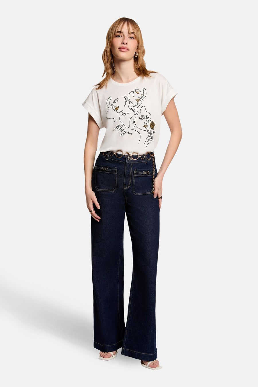Wit T-shirt met korte mouwen van Morgan de Toi met gezichtenprint, gedragen met een high-waisted jeans en een kettingriem.