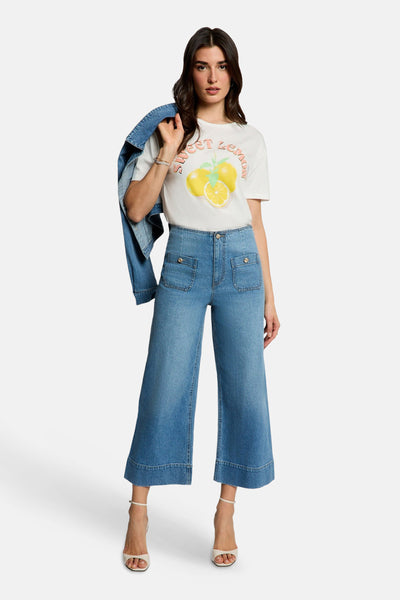 T-shirt blanc à manches courtes de Morgan de Toi, imprimé citron, porté avec un jean taille haute et des talons.