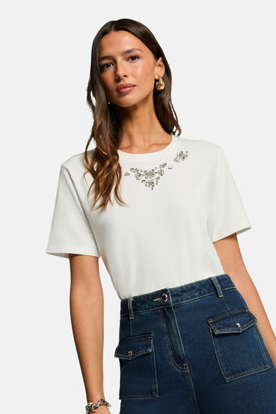 T-shirt blanc à manches courtes de Morgan de Toi, orné de strass décoratifs, porté avec un pantalon en jean bleu.