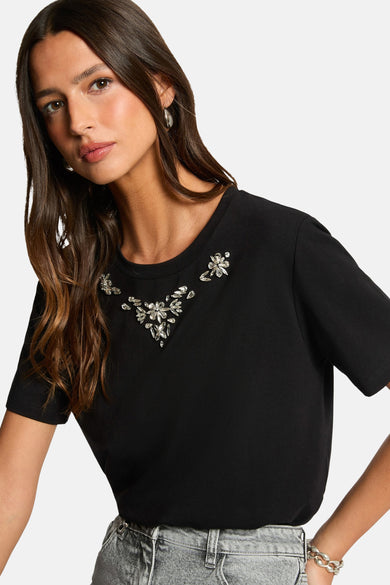 Zwart T-shirt met korte mouwen van Morgan de Toi, versierd met decoratieve strassteentjes rond de halslijn, gedragen met een verbleekte spijkerbroek en zilveren oorbellen.