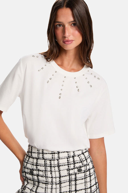 T-shirt blanc à manches courtes de Morgan de Toi orné de strass sur le devant, porté avec une jupe à carreaux.
