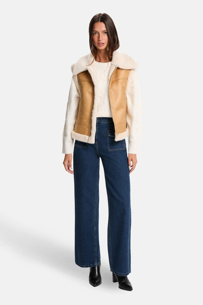 Cognac mouwloos vest van Morgan de Toi, met crème imitatiebontkraag, gedragen over een trui en een blauwe jeans.