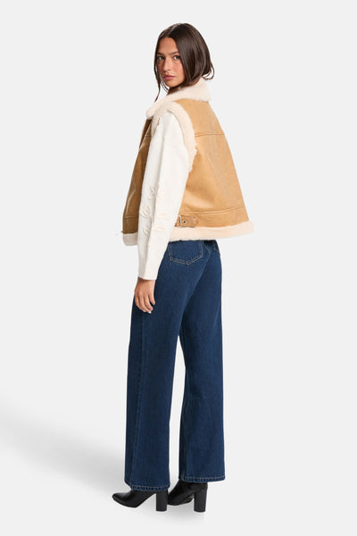Veste sans manches cognac de Morgan de Toi avec col en fausse fourrure, portée avec un pull et un jean amples.