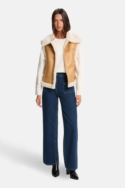 Cognac mouwloos vest van Morgan de Toi, met imitatiebont voering, gedragen over een crèmekleurige trui en een wijde jeans.