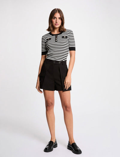 Black round-neck sweater with white horizontal stripes, short sleeves, and front buttons, worn with black shorts and loafers, full-body lifestyle view