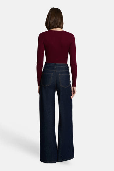 Burgundy ribbed V-neck long-sleeve sweater, back view, paired with dark wide-leg jeans, model wearing delicate necklace
