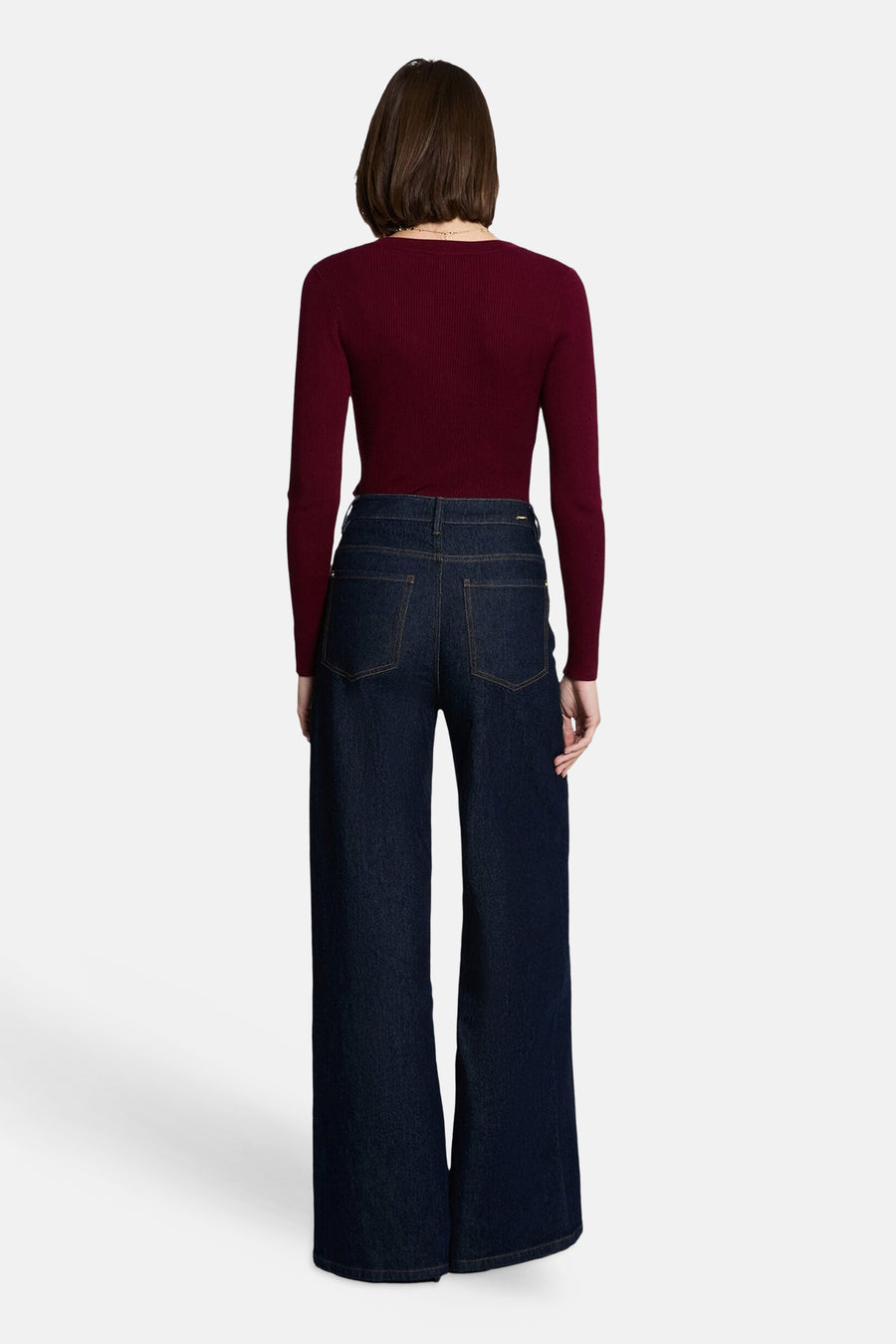 Burgundy ribbed V-neck long-sleeve sweater, back view, paired with dark wide-leg jeans, model wearing delicate necklace