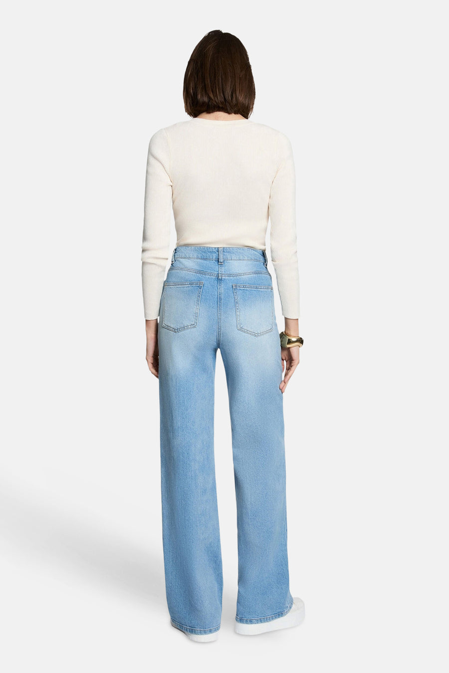 Ecru ribbed V-neck sweater back view with long sleeves, worn with light blue wide-leg jeans and white sneakers.