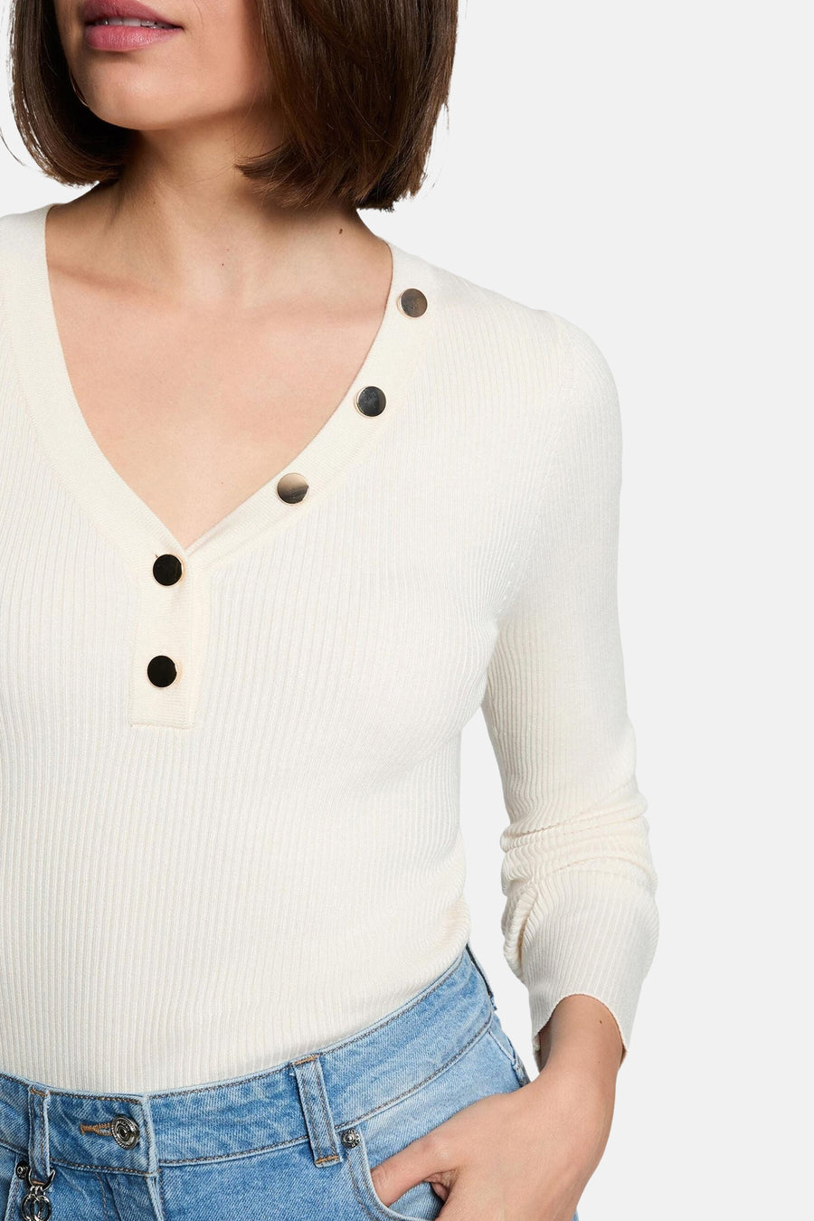 Ecru ribbed V-neck sweater with black buttons, worn with blue jeans, cropped front view