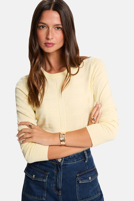 Pull à col rond jaune de Morgan de Toi avec manches longues, porté avec un pantalon taille haute.