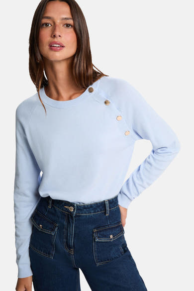 Pull à col rond bleu de Morgan de Toi avec des boutons dorés sur l'épaule, porté avec un jean taille haute.
