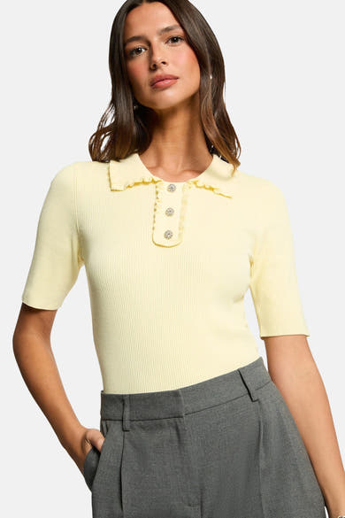 Polo jaune van Morgan de Toi, avec col et patte de boutonnage volantés, porté avec un pantalon gris.
