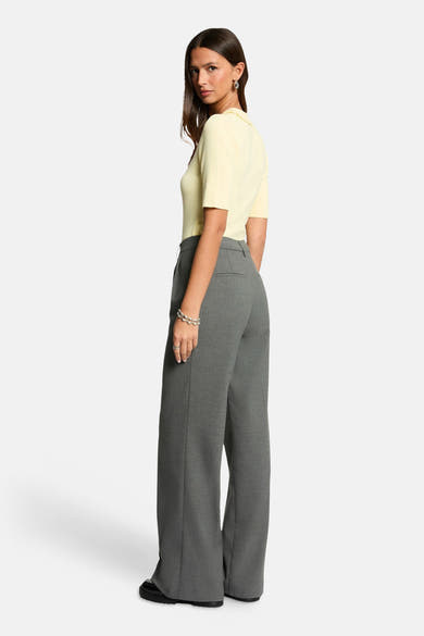 Polo jaune clair de Morgan de Toi, en maille côtelée, porté avec un pantalon gris taille haute et des bijoux argentés.