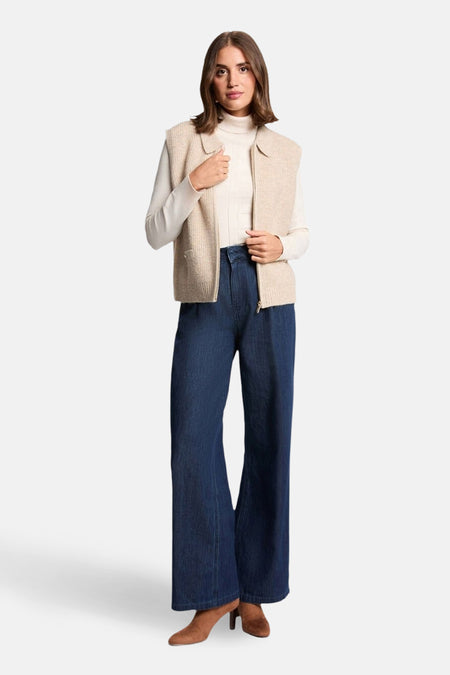 Gilet beige zippé de Morgan de Toi, porté sur un pull blanc à col roulé et un jean large bleu.
