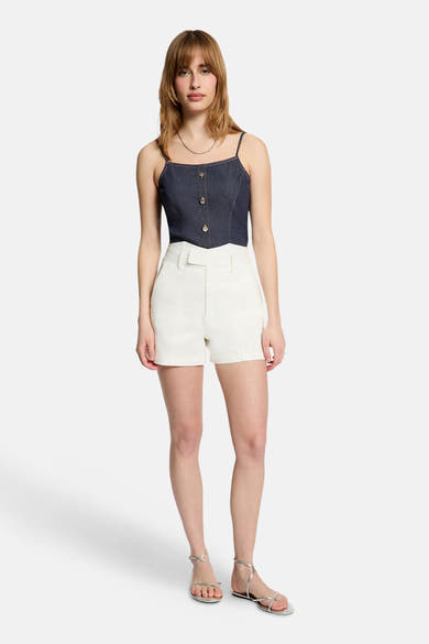Top en jean bleu foncé de Morgan de Toi avec bretelles fines, boutons fantaisie et surpiqûres claires, porté avec un short écru et des sandales argentées.