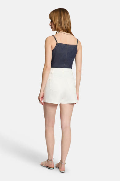 Top en jean bleu foncé de Morgan de Toi, avec fines bretelles et coutures, porté de dos avec un short blanc et des sandales.