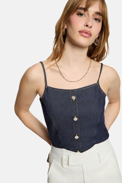 Top en jean bleu foncé de Morgan de Toi, à fines bretelles et boutons décoratifs, porté avec un pantalon blanc.