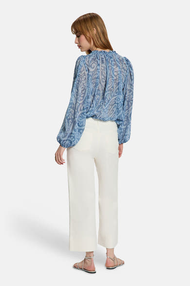 Chemisier bleu à manches longues de Morgan de Toi, avec un motif paisley, porté avec un pantalon blanc.