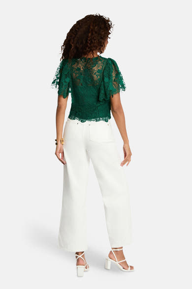 Chemisier vert en dentelle de Morgan de Toi, avec manches courtes flottantes et pantalon blanc.