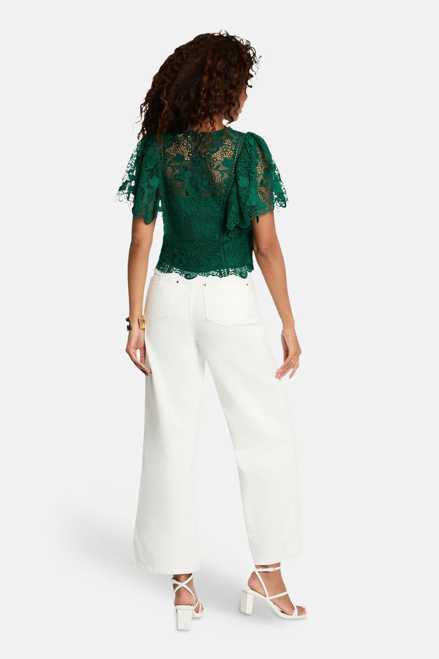 Chemisier vert en dentelle de Morgan de Toi, avec manches courtes flottantes et pantalon blanc.