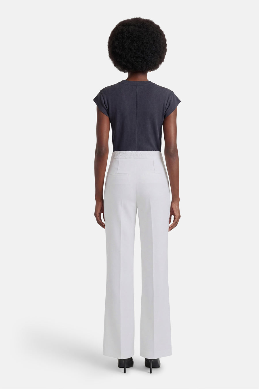 Witte pantalon van Morgan de Toi, wijde pasvorm met hoge taille, van achteren gezien met een donkergrijs topje en zwarte hakken.