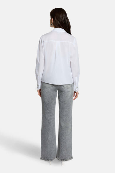 Jean large gris moyen de Morgan de Toi, coupe droite, porté avec une chemise blanche à manches longues.