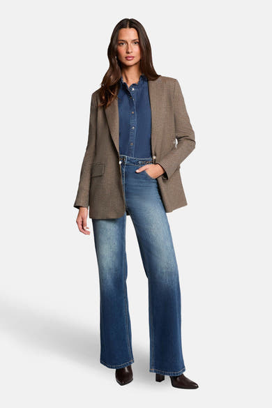 Wijde spijkerbroek in donkerblauw denim van Morgan de Toi, met wassing en uitlopende pijpen, gedragen met een overhemd en een blazer.