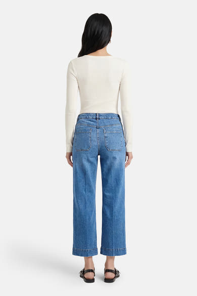 Jean large bleu denim par CAROLL, coupe cropped et ourlet revers, porté avec un haut blanc et des sandales noires.