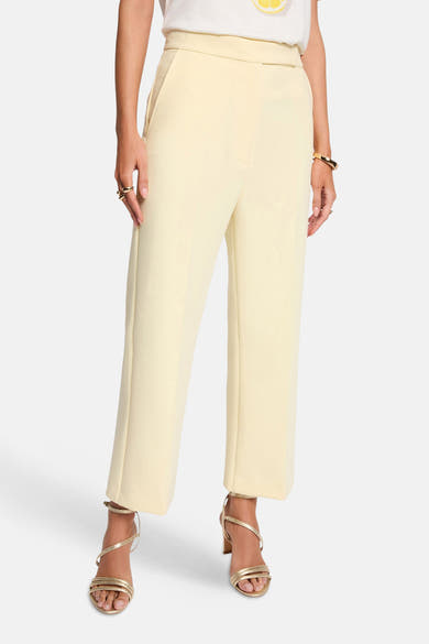 Pantalon jaune de Morgan de Toi, coupe droite, porté avec des sandales dorées et un bracelet doré.

