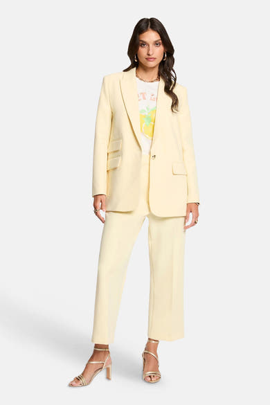 Pantalon jaune de Morgan de Toi, coupe droite et longueur cheville, porté avec un t-shirt imprimé citron et des sandales dorées.