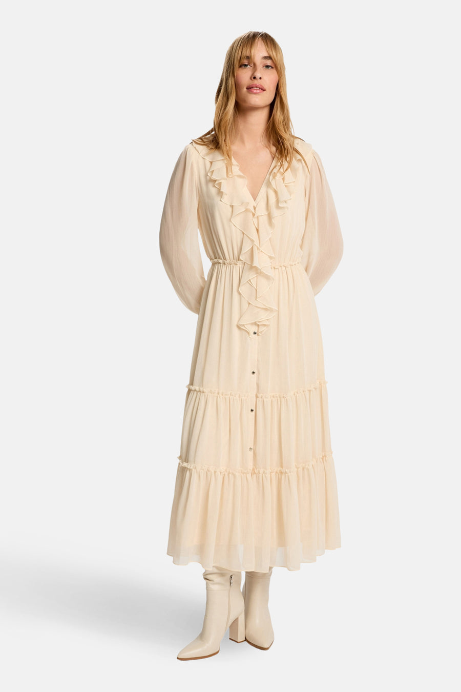 Lange beige jurk met lange mouwen van Morgan de Toi, met ruches en knoopdetails, gedragen met lichte laarzen.