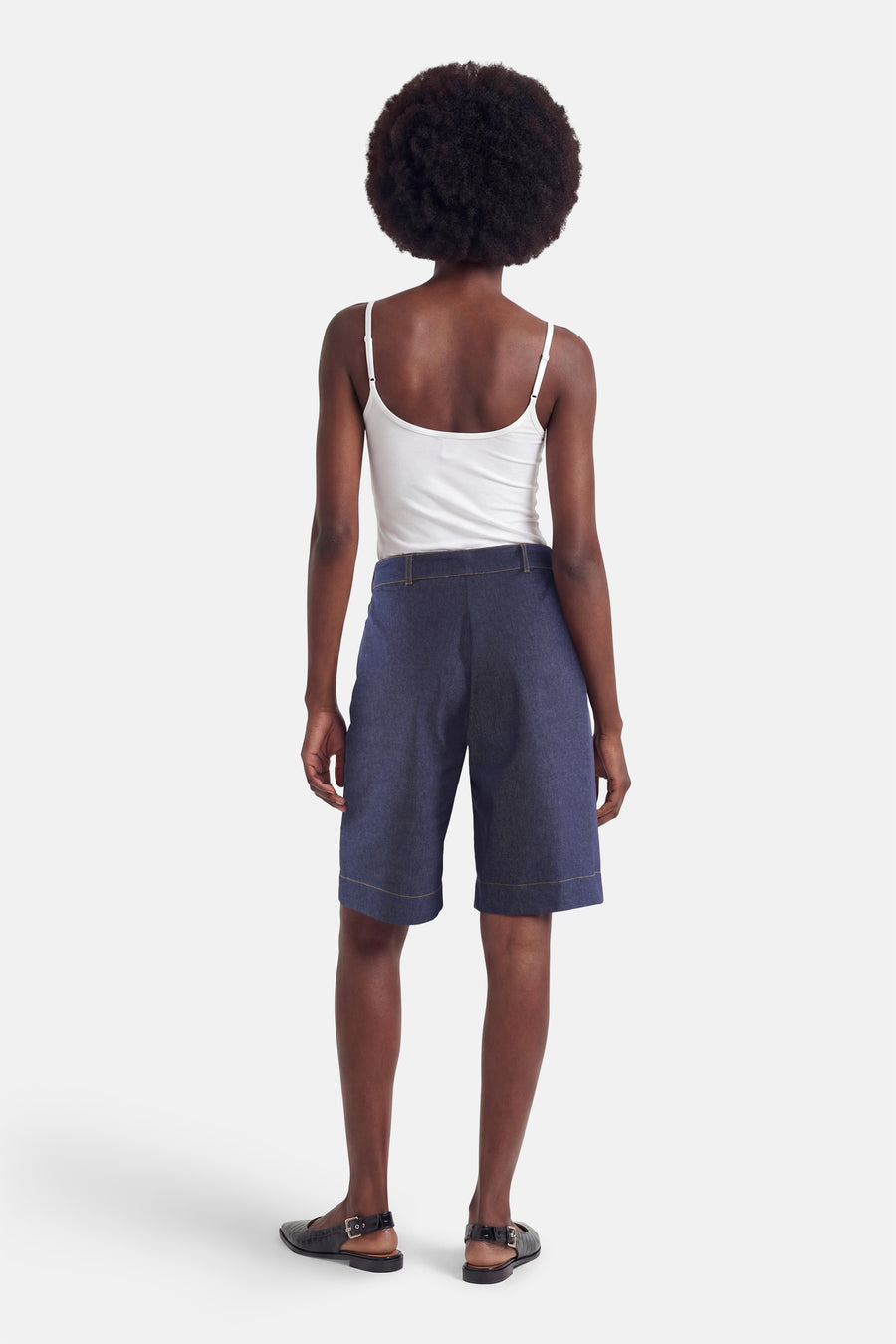 Donkerblauwe spijkerbroekshorts van Morgan de Toi met contrasterende stiksels, van achteren gedragen met een witte tanktop en zwarte platte schoenen.