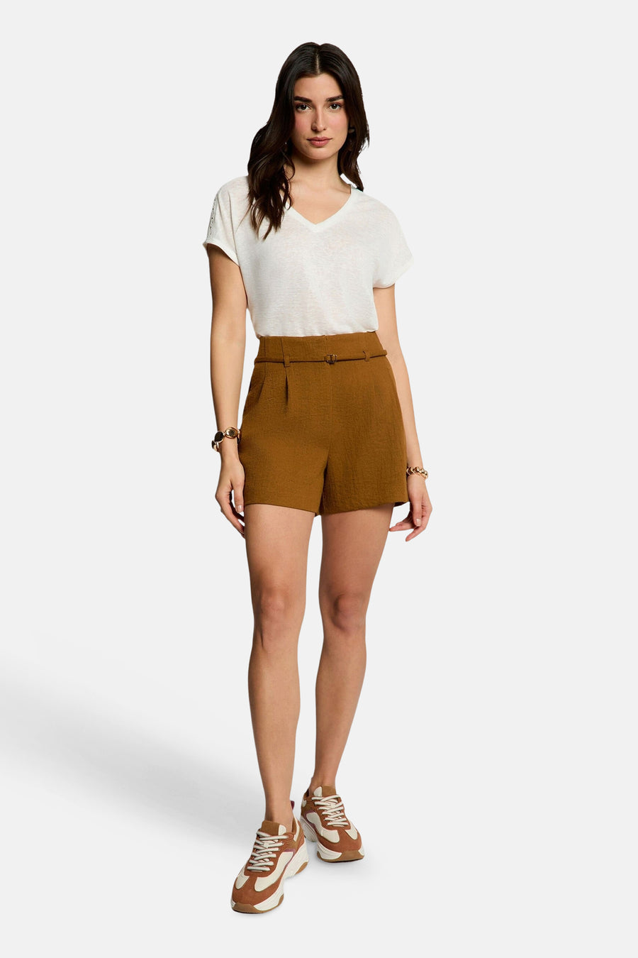 Korte, getextureerde bruine broek van Morgan de Toi, hoge taille met ceintuur, gedragen met een wit T-shirt en tweekleurige sneakers.