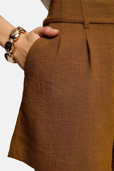 Korte bruine Morgan de Toi, in getextureerde stof, met een hand in de zak en een gouden armband.